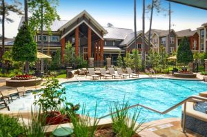A serene swimming pool nestled amidst lounge chairs and trees, offering a tranquil oasis for residents of apartments in The Woodlands, TX.
