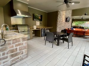 A stunning outdoor kitchen and dining area with a cozy fireplace, perfect for residents of apartments in The Woodlands TX.