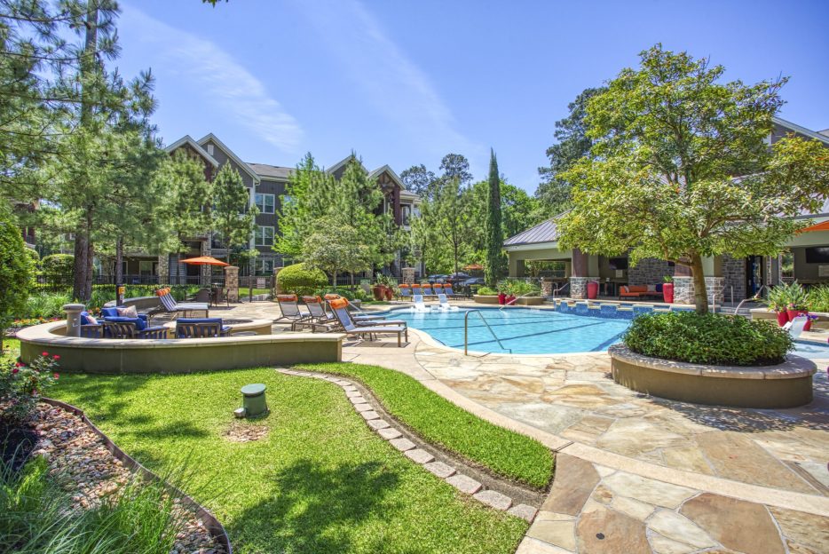 An apartment complex in The Woodlands TX with a swimming pool and lounge chairs.