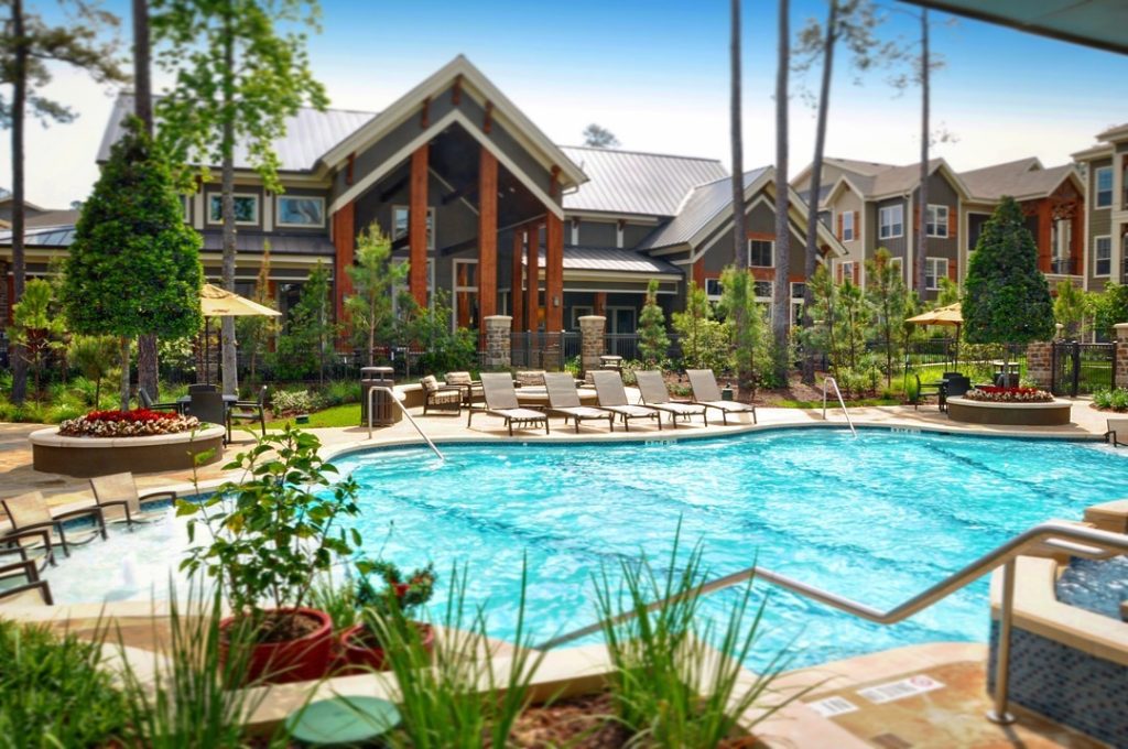 Apartments For Rent in The Woodlands A serene outdoor pool area with lounge chairs, umbrellas, and lush greenery complements the residential complex featuring multi-story buildings, where you can find both one-bedroom for rent in The Woodlands and two-bedroom apartments for rent in The Woodlands. The Woodlands Lodge Apartments 2500 S Millbend Dr, The Woodlands, TX 77380